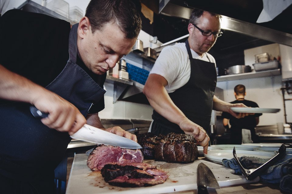 A chef at Lish Foods is slicing into freshly prepared meat.