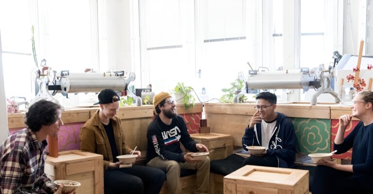 Guests enjoying Lish event catering bowls in a bright office space with modern wooden furniture.