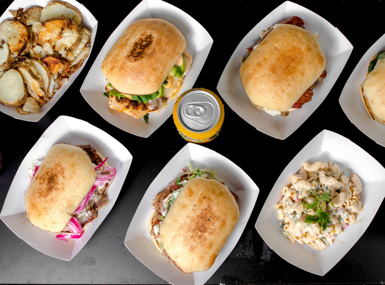 A variety of Lish catering sandwiches, sides, and a soda are laid out on a black surface.
