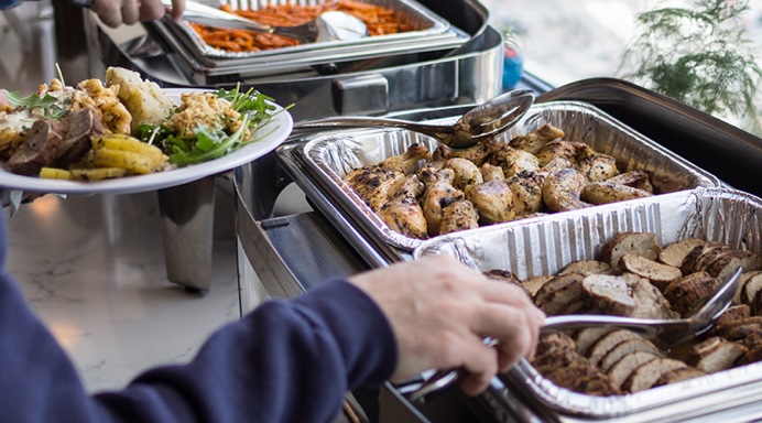 Close-up of people serving food from buffet trays of chicken, bread, and salad from the Lish office catering setup.