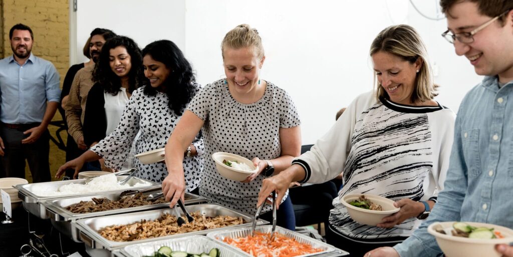 Coworkers serving themselves with a breakfast buffet from Lish Catering with healthy food options in the office.