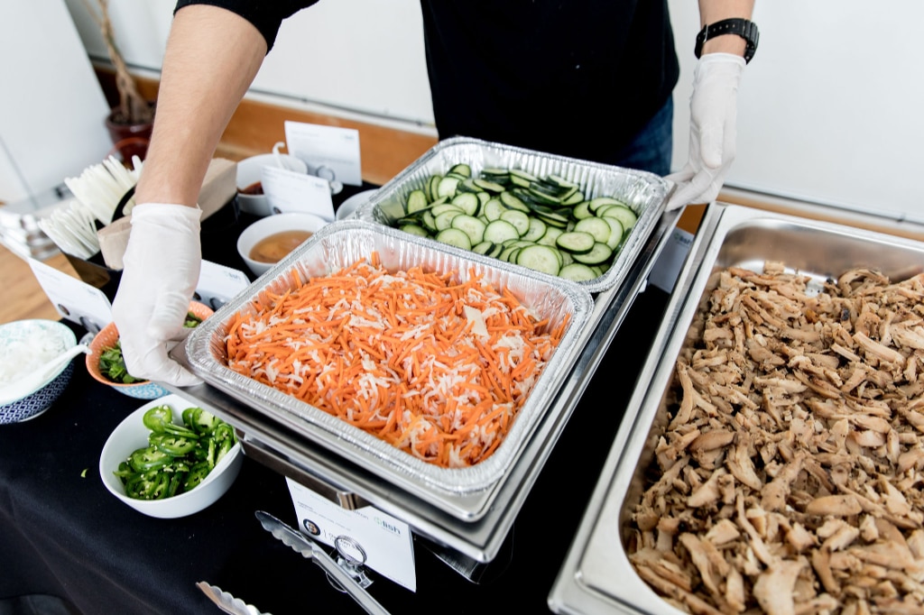 A person setting up a fresh salad tray at a Seattle corporate event catered by Lish.