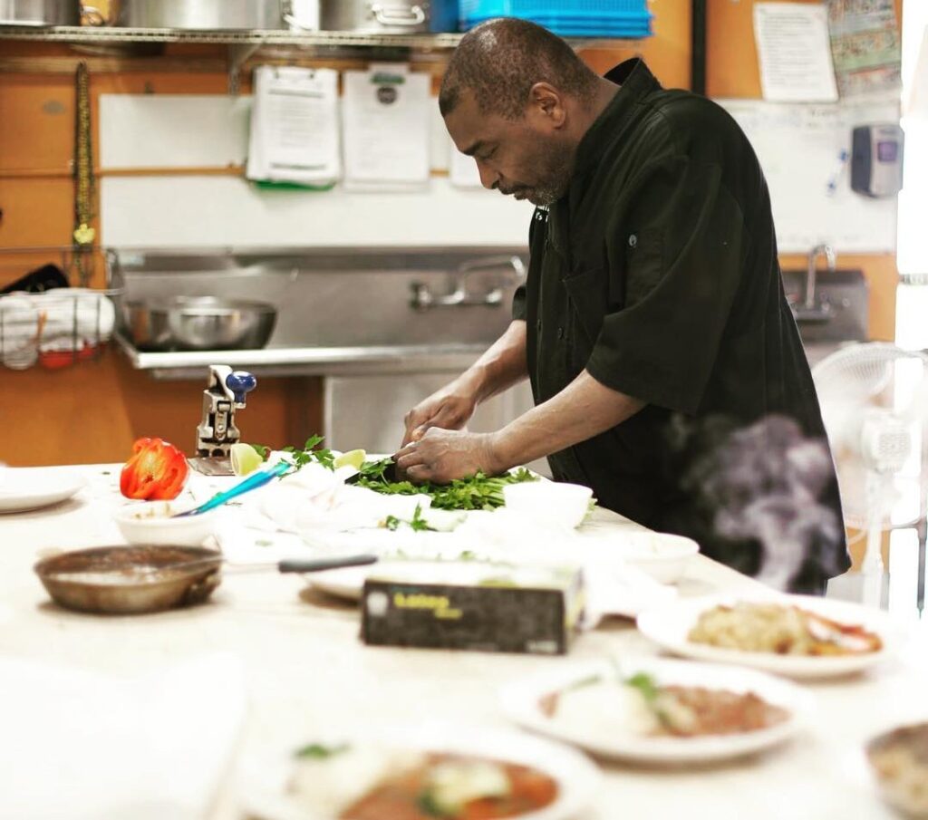  Lish Chef in a black coat, chopping leafy greens in the kitchen, preparing to cook.