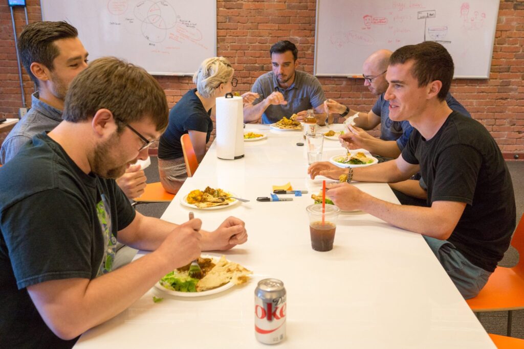 A group of coworkers enjoying plated meals from Lishfood together at a long table in an office setting.