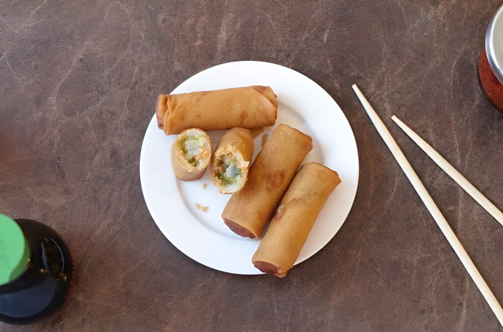 Four crispy spring rolls catered by Lish served on a white plate with chopsticks.