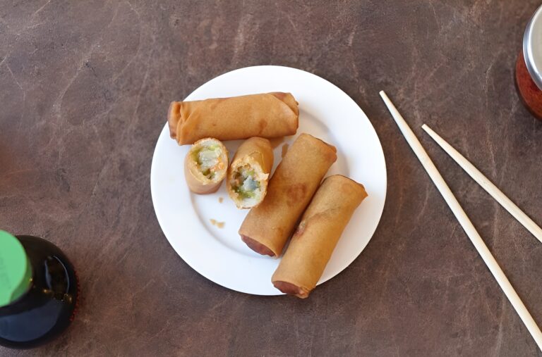 Four crispy spring rolls catered by Lish served on a white plate with chopsticks.