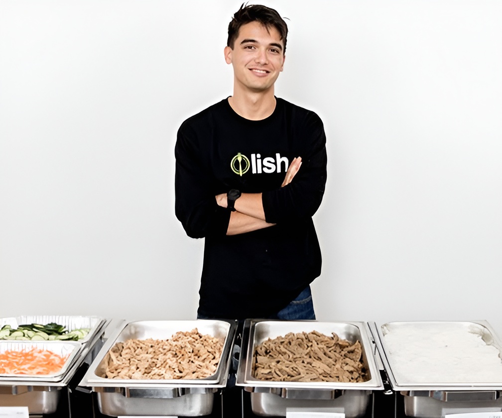 A Lish employee standing behind buffet trays of BBQ food at a catering event.
