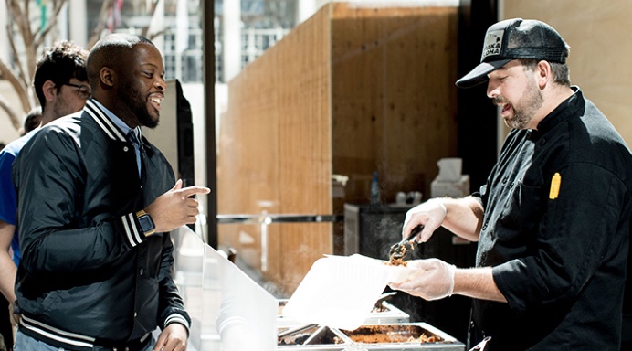An office employee chatting with a Lish caterer while serving food from a buffet line.