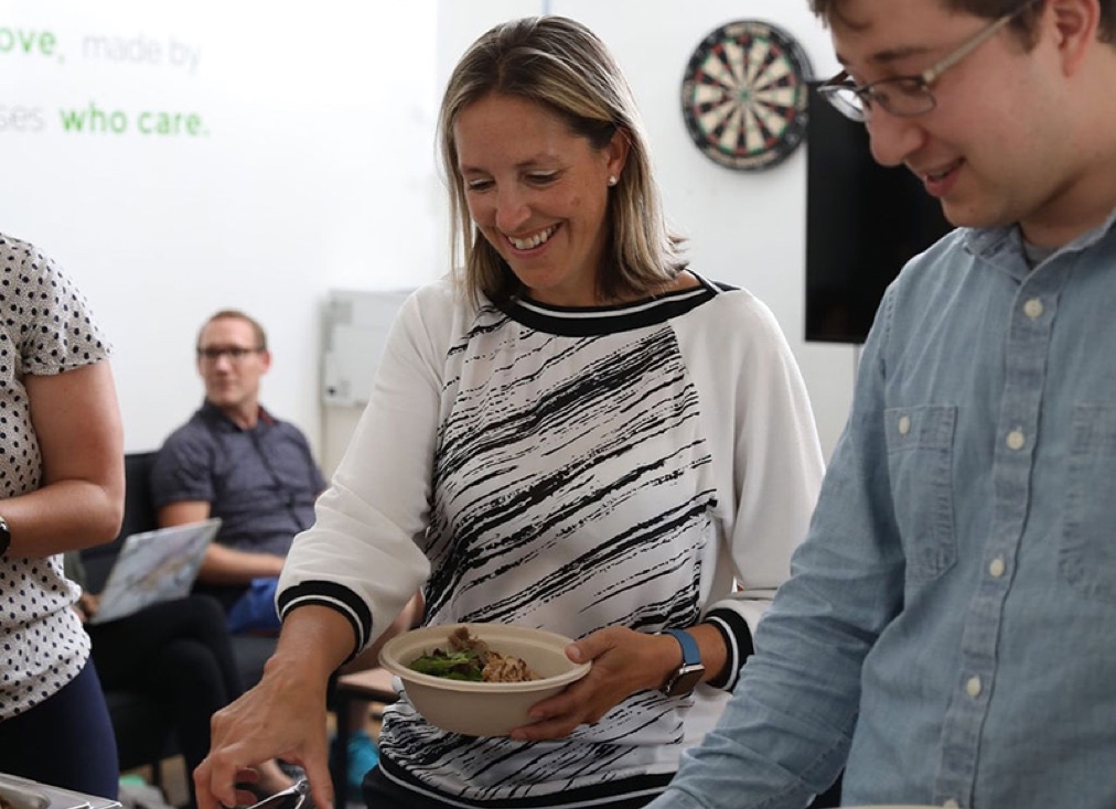Two coworkers serving themselves Mediterranean dishes from Lish catering trays during an office lunch.
