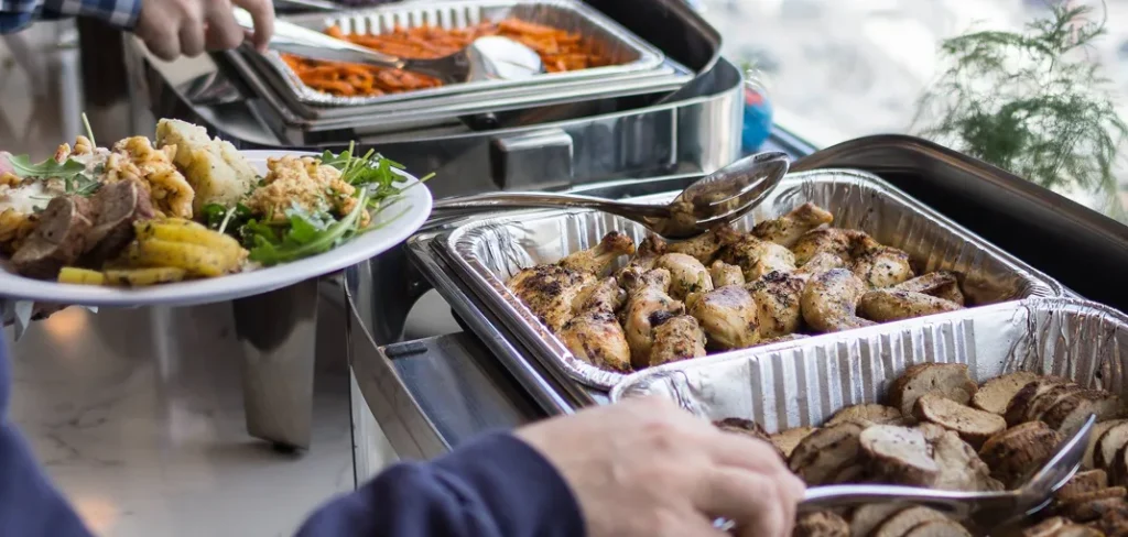 An employee serving himself roasted chicken and sides from buffet trays. 