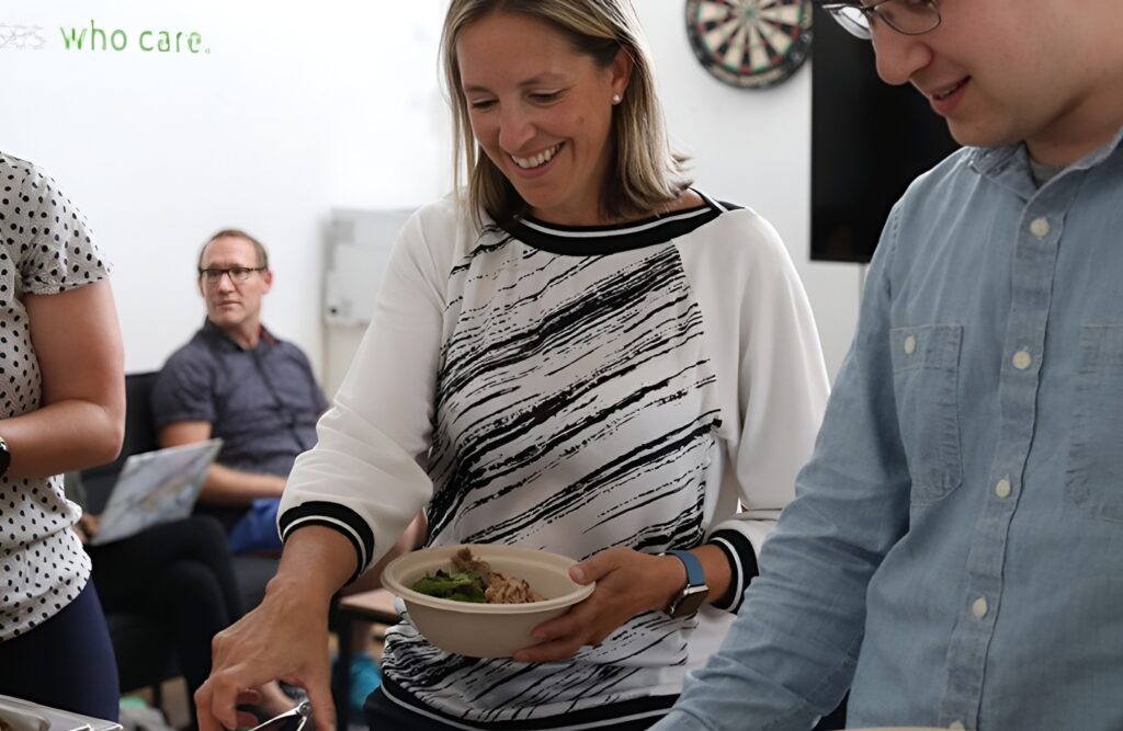 Employees smiling and holding bowls of food at an office catering by Lish.