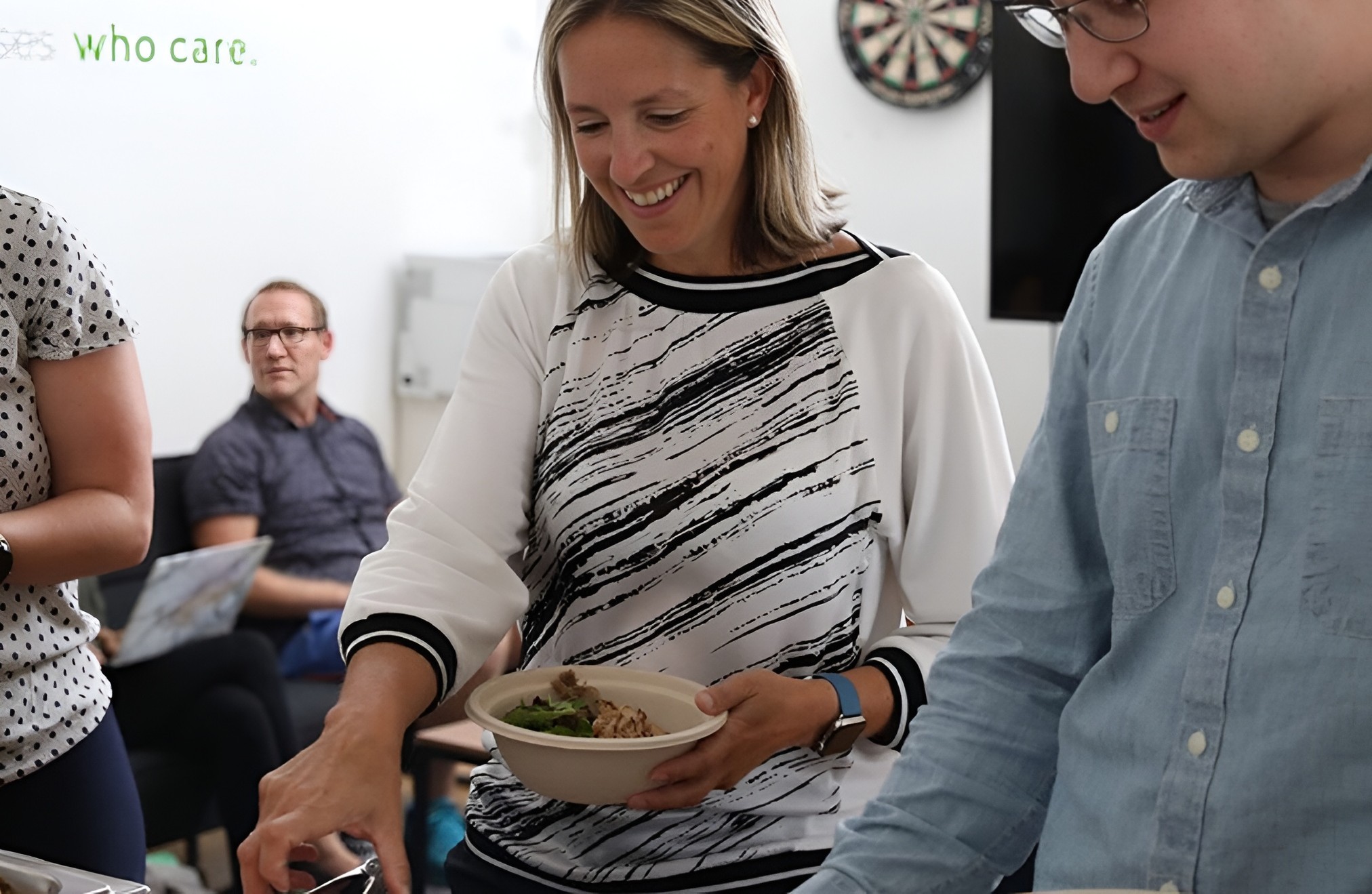 Employees smiling and holding bowls of food at an office catering by Lish.