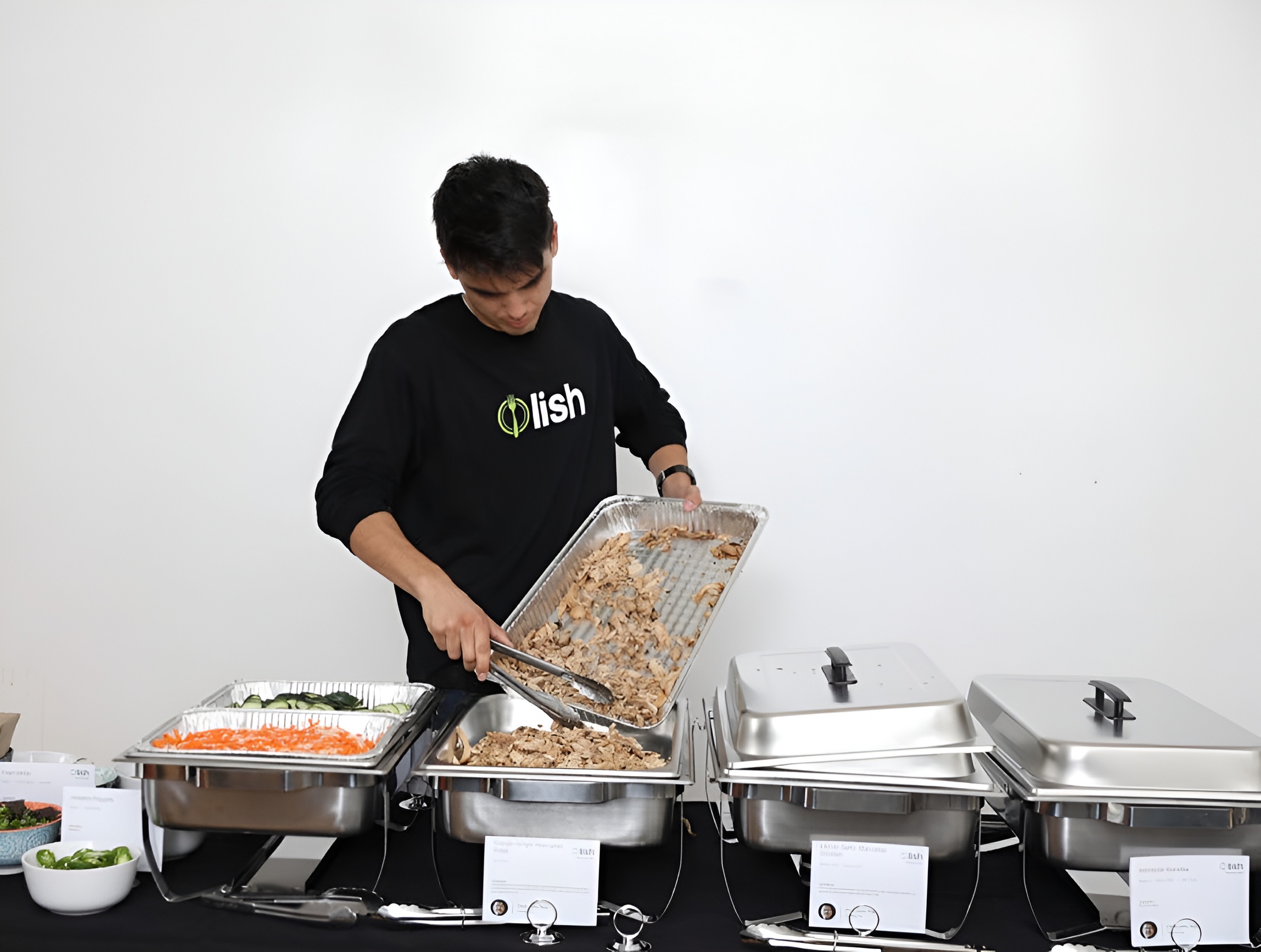 A Lish employee transferring food from dishes to a buffet setup for an office lunch.